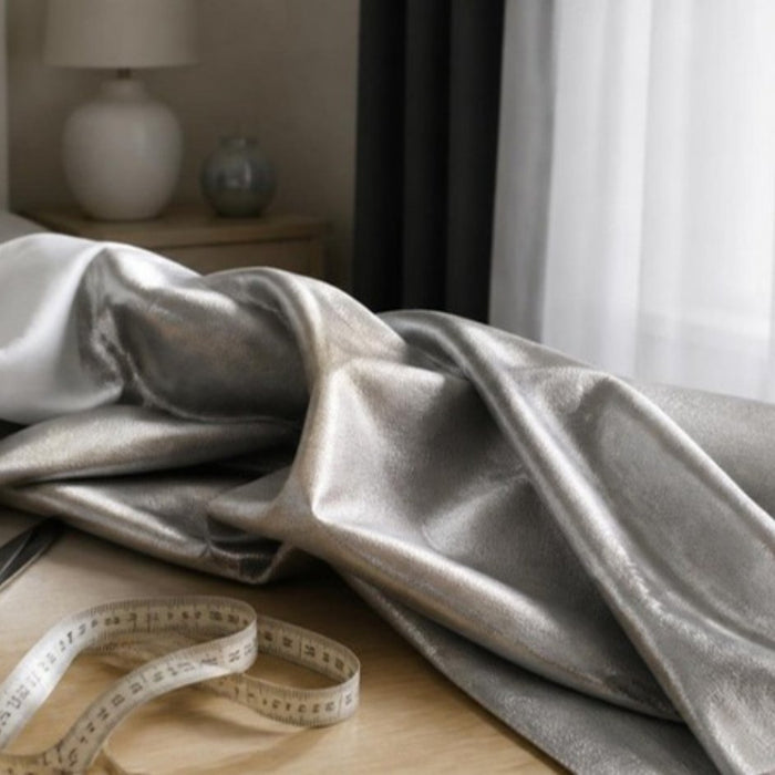 Roll of silver EMF shielding fabric on a sewing table beside a bedroom window with sheer curtains