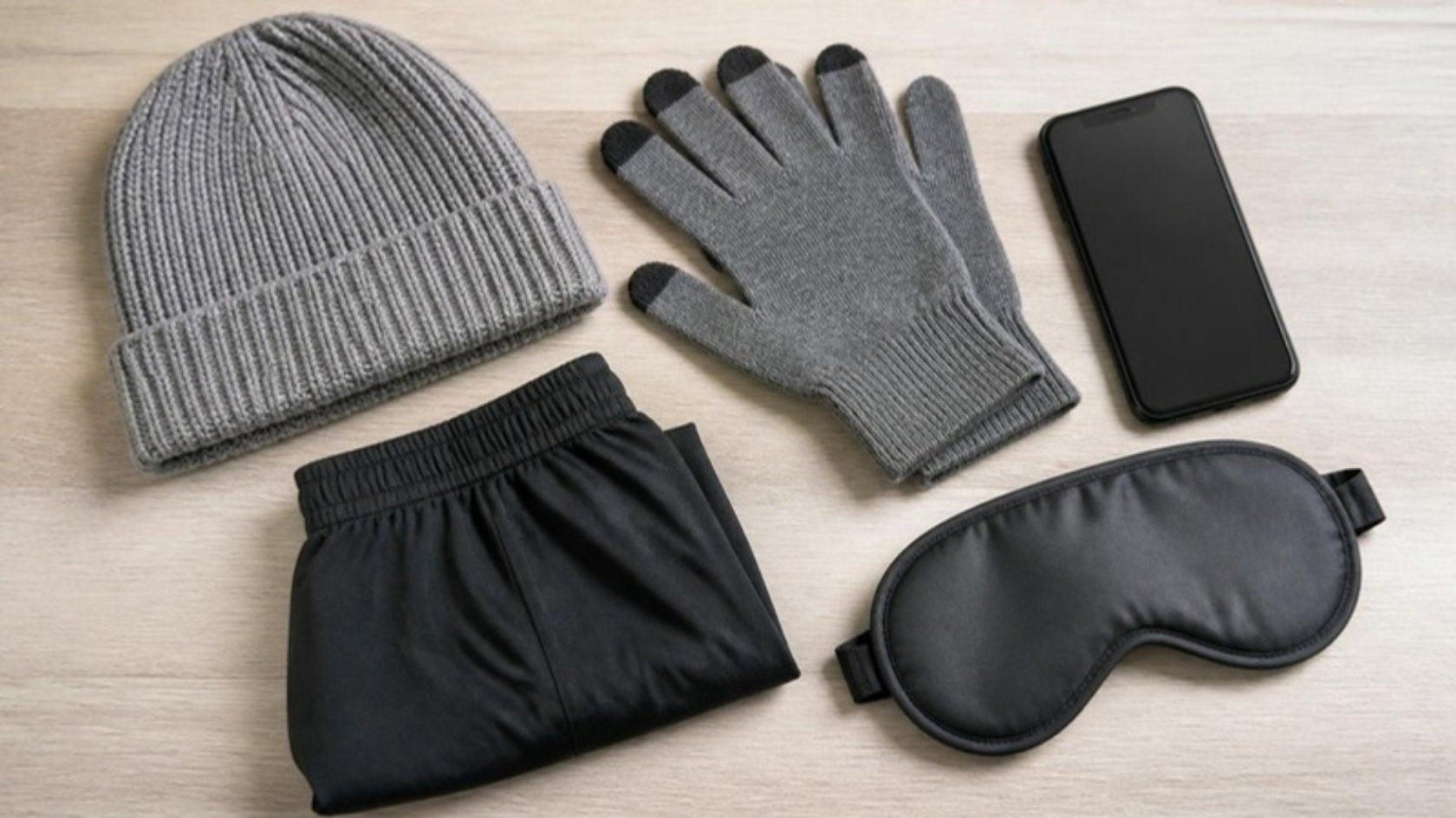 Flat lay of EMF protection clothing: shielding beanie, touchscreen gloves, shorts and sleep mask beside a smartphone